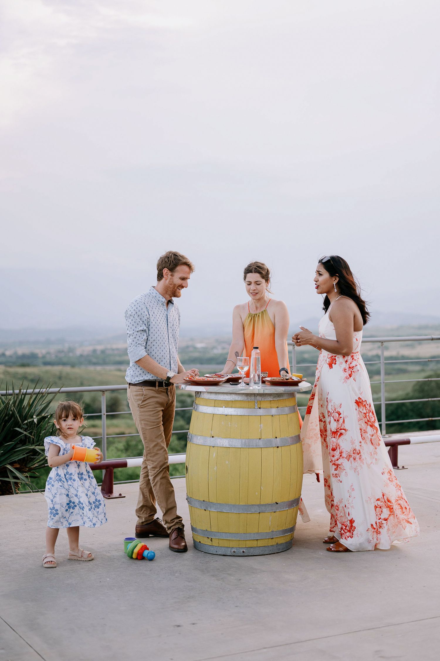 Family gathering on an outdoor terrace with wine barrels and a scenic mountain view in the background.