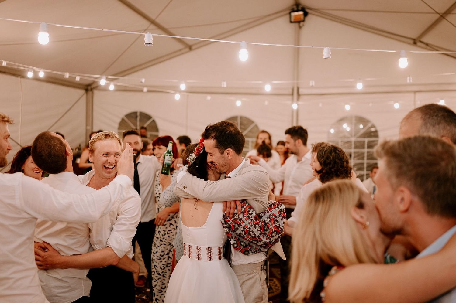 Wedding reception dance party with guests celebrating under string lights.
