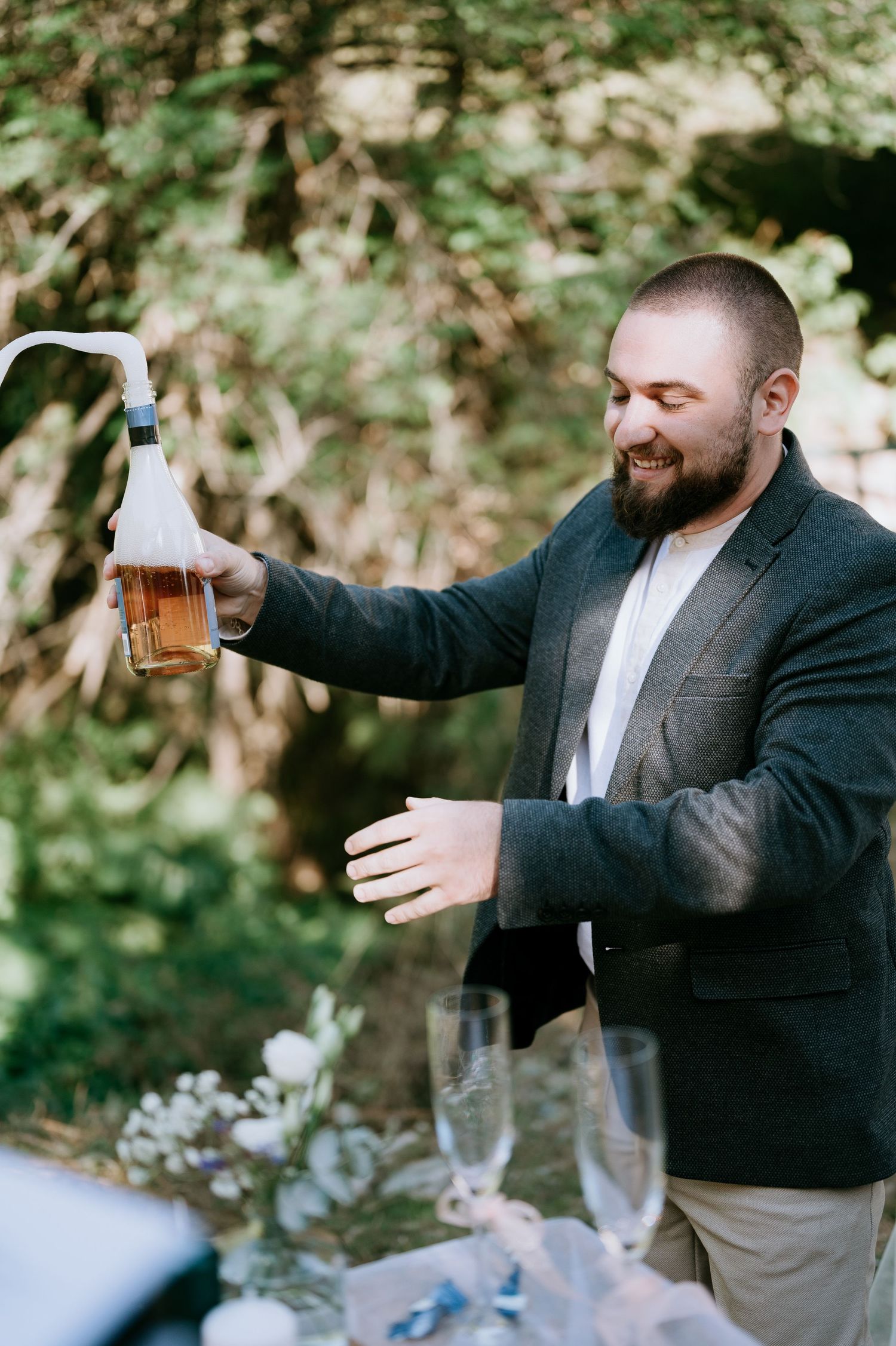 A person in a blazer joyfully pours a beverage at an outdoor celebration.