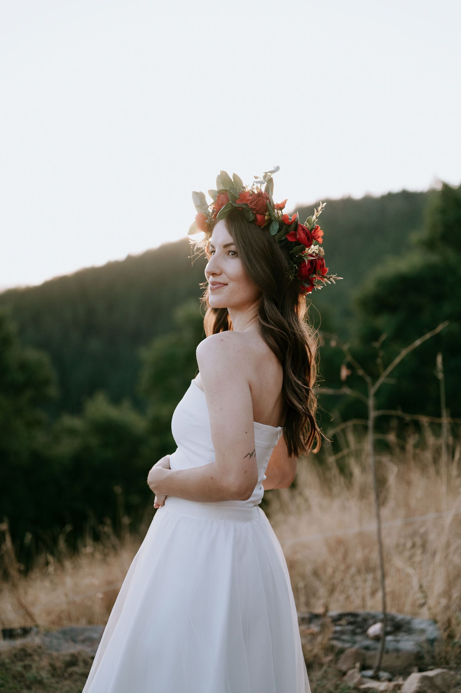 A joyful moment captured in a white wedding dress with red floral crown against mountains at sunset.
