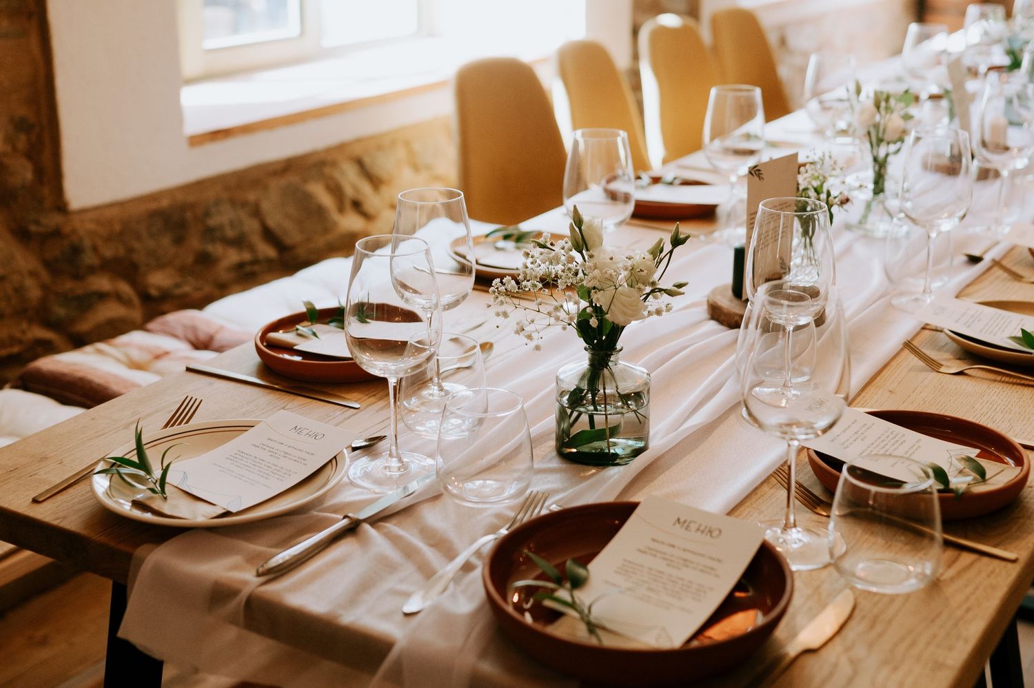 Close-up of elegant place settings with wine glasses and white linens on wooden tables.