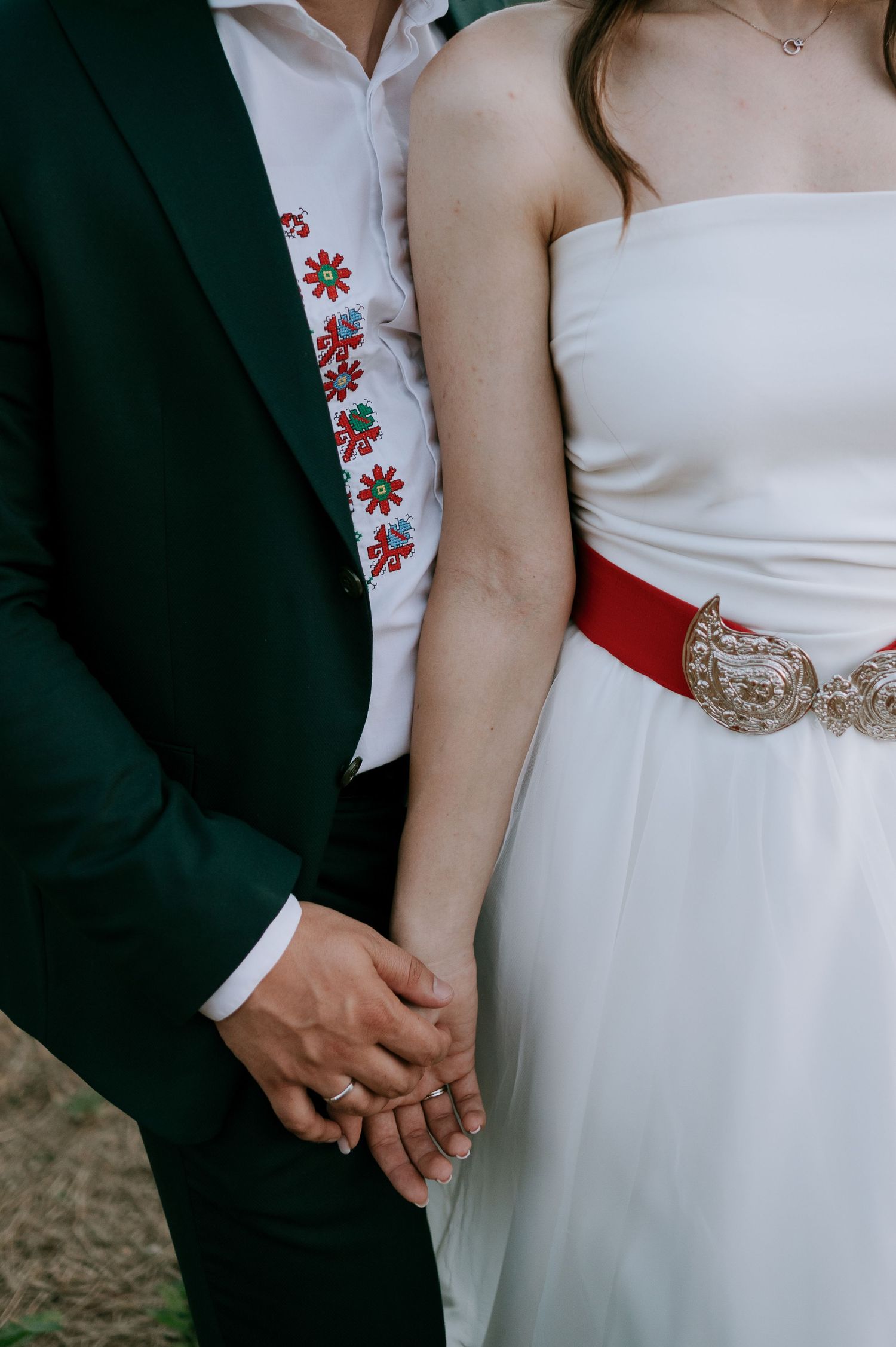 Close-up details of wedding attire showing embroidered jacket and crystal belt.