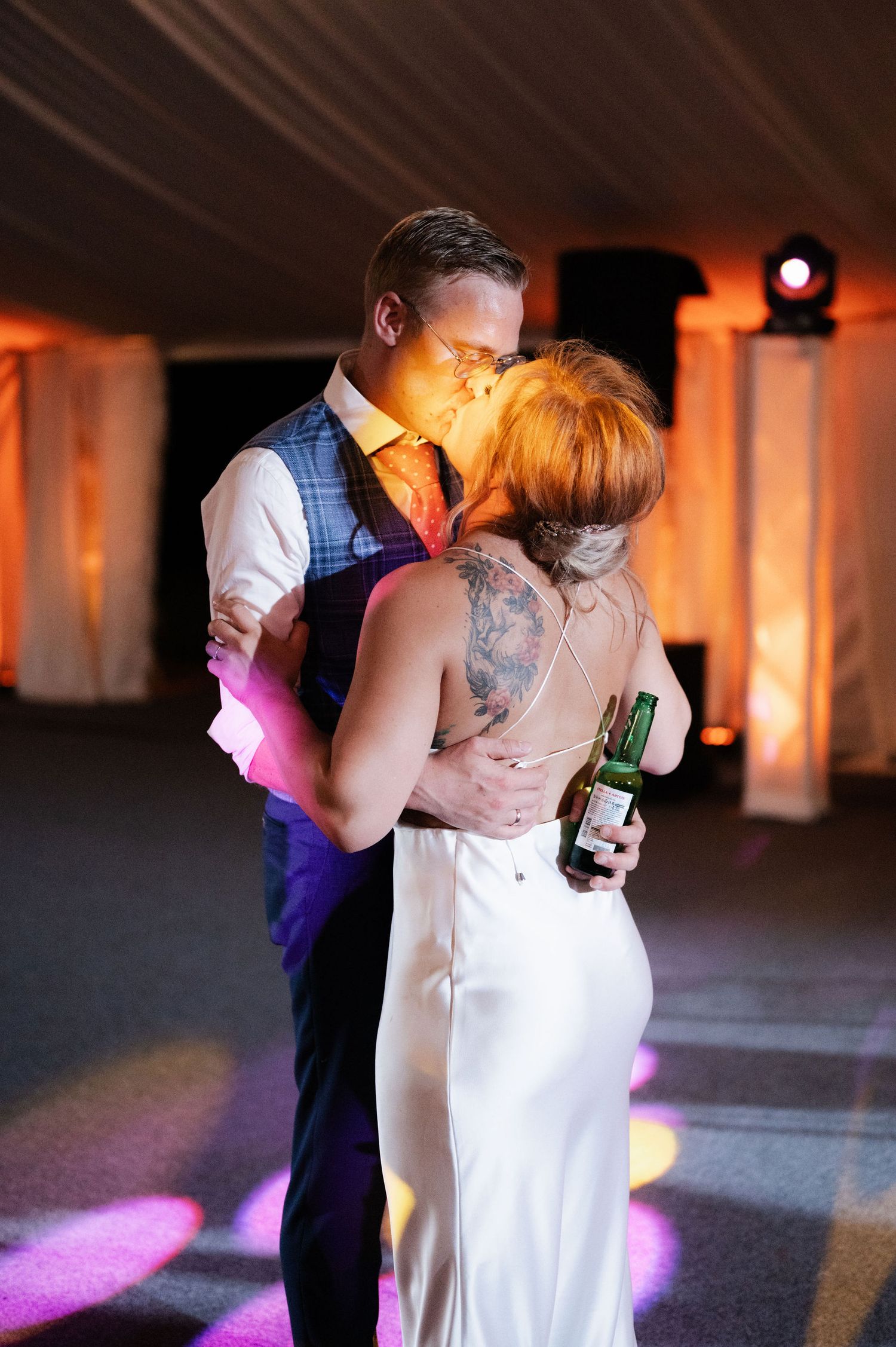 A couple shares a romantic dance at their wedding reception with soft orange lighting and pink accents on the floor.