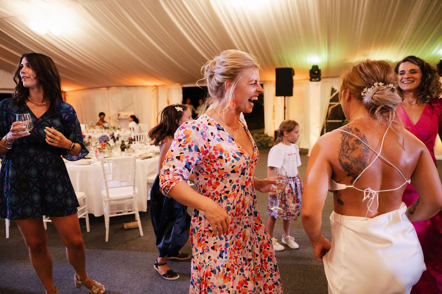 Wedding guests dance and celebrate together on an illuminated dance floor at an indoor reception venue.