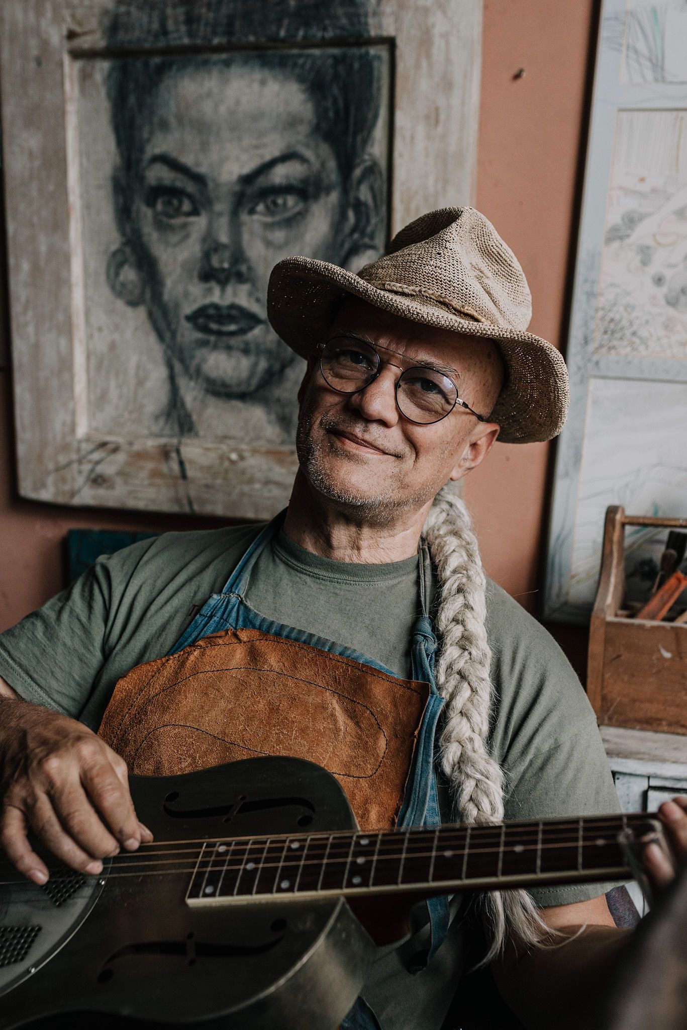 Artist's studio with guitar player seated among framed portrait sketches.