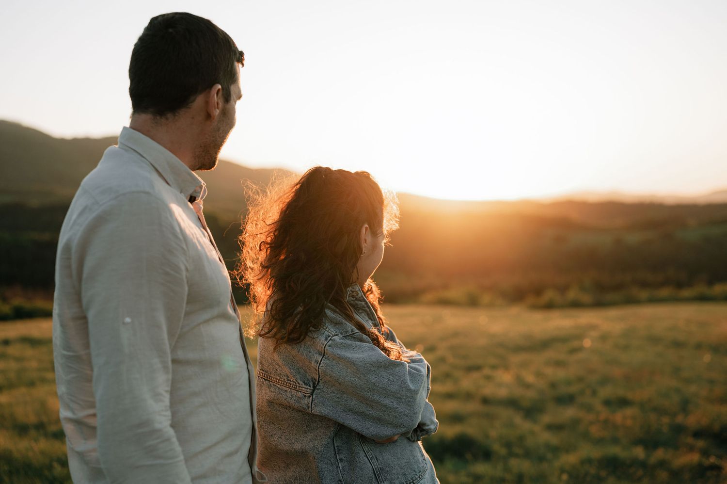 Couple embraces in golden sunlit field during sunset photoshoot.