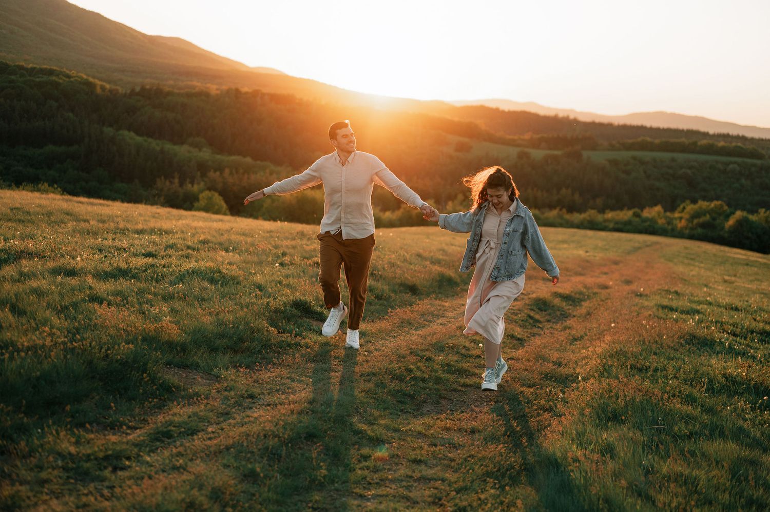 A couple dances together on a grassy hillside during golden hour sunset.