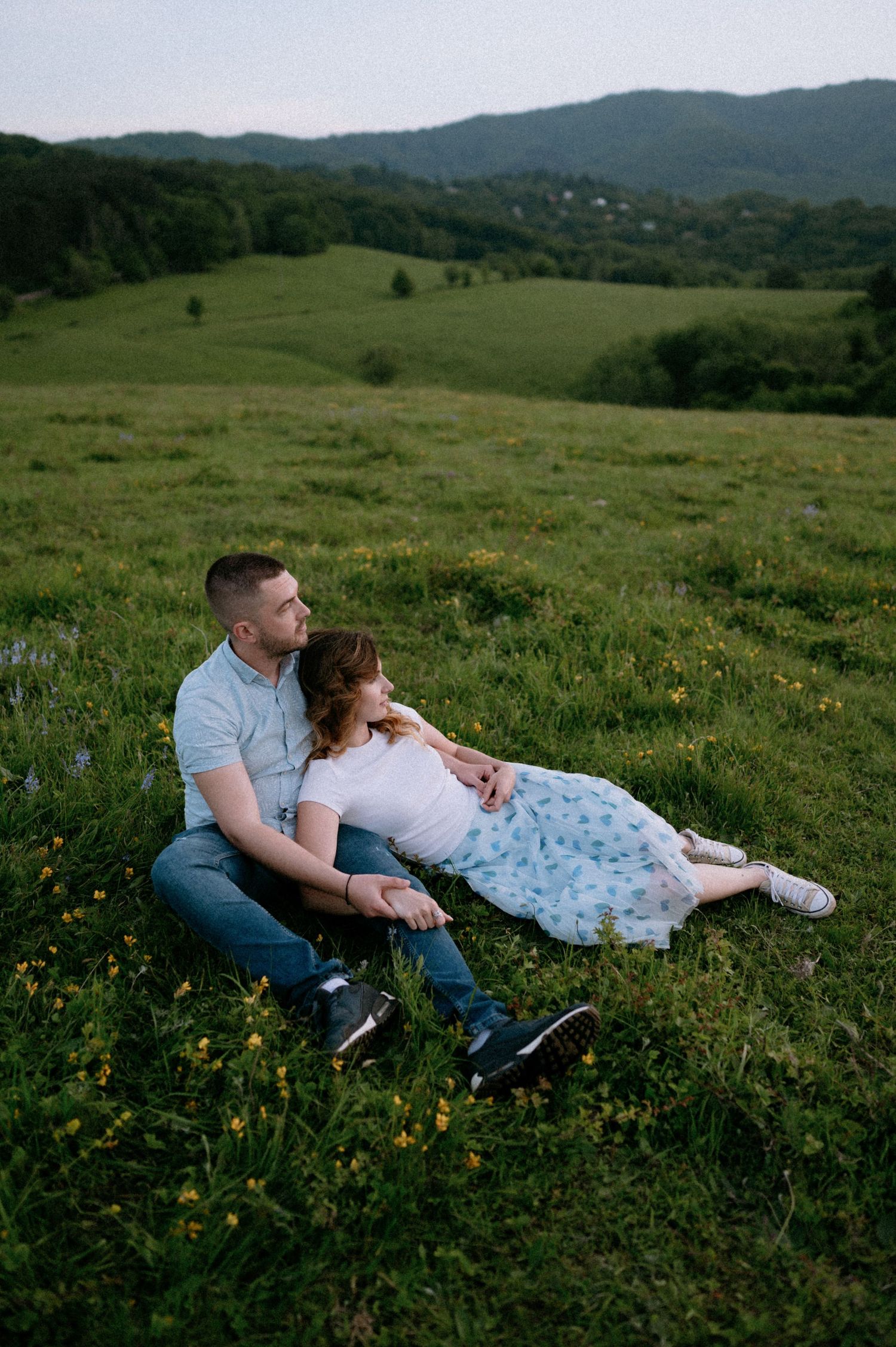 A couple reclines together in a mountain meadow surrounded by spring flowers.