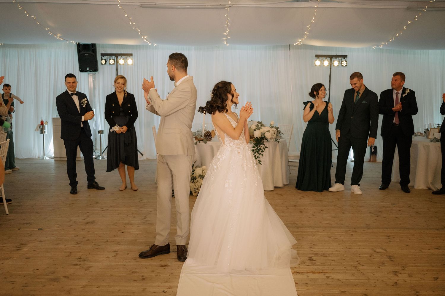 Bride and groom share first dance at elegant wedding reception with guests applauding around them.