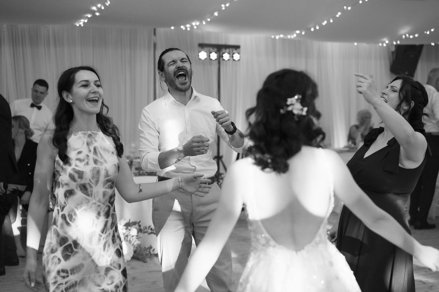 Black and white wedding reception photo of guests laughing and dancing joyfully on the dance floor.