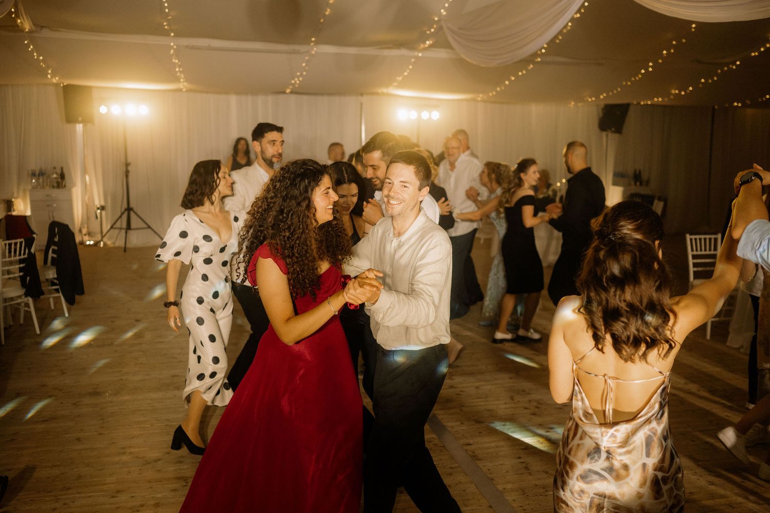 Couples dancing joyfully at a wedding reception in a decorated venue with warm ambient lighting.