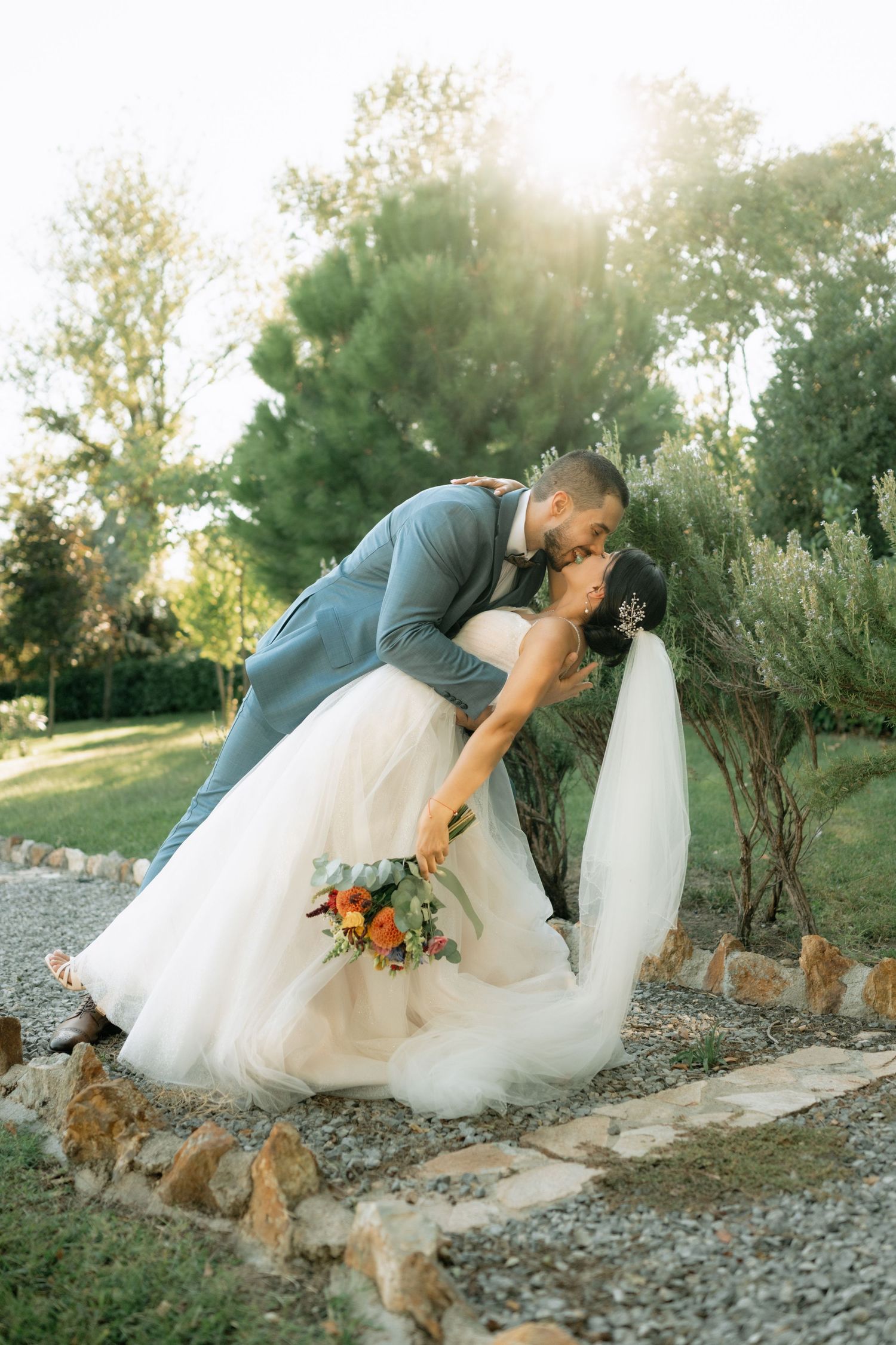 A romantic wedding photo series showing a couple dipping in an outdoor setting with a dog joining the moment.