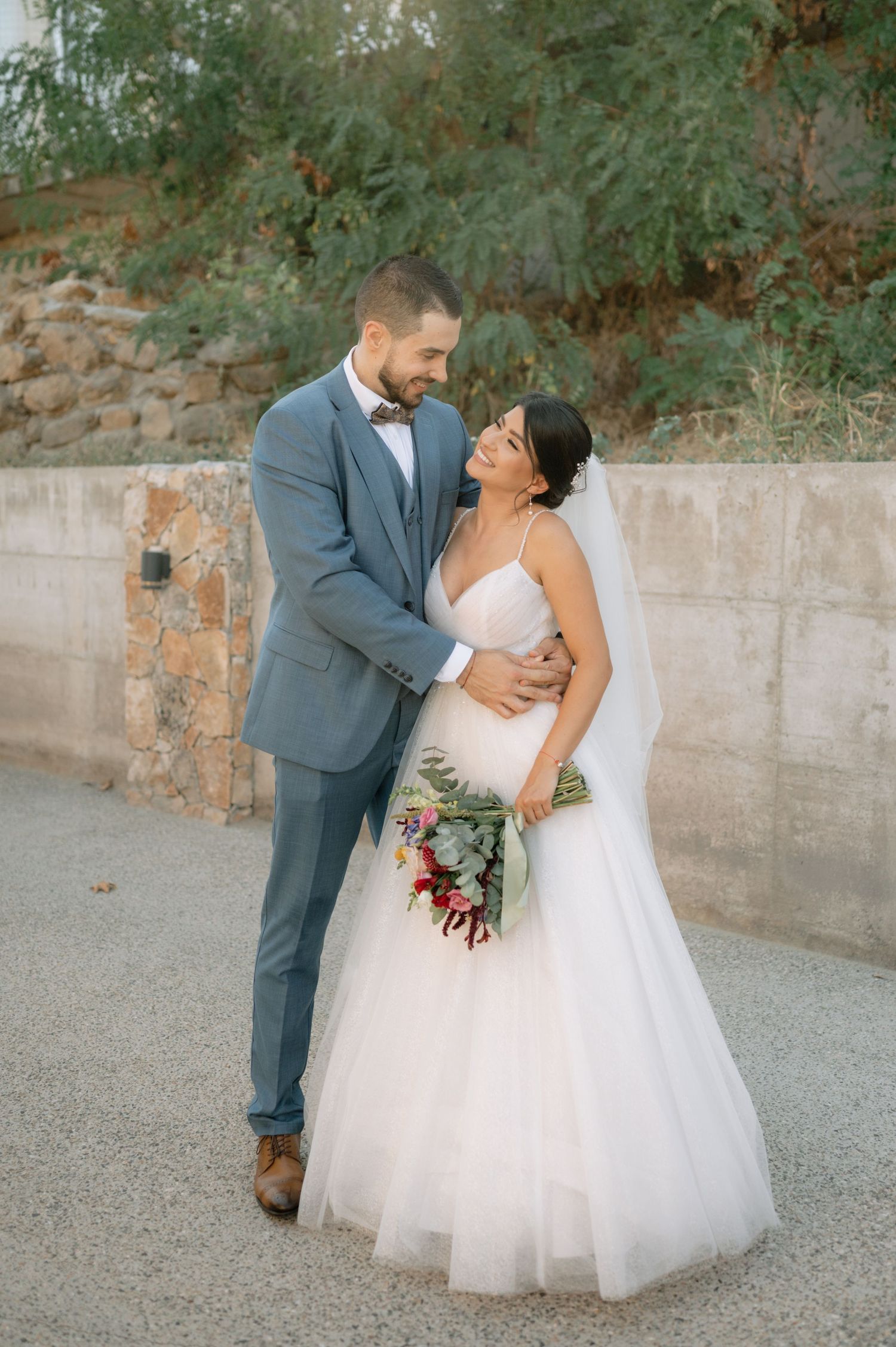 Romantic wedding couple shares intimate moments in four sequential photos against a stone wall and greenery backdrop.