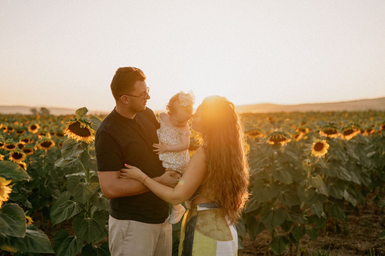 Family with baby enjoying golden hour sunset in a vibrant sunflower field.