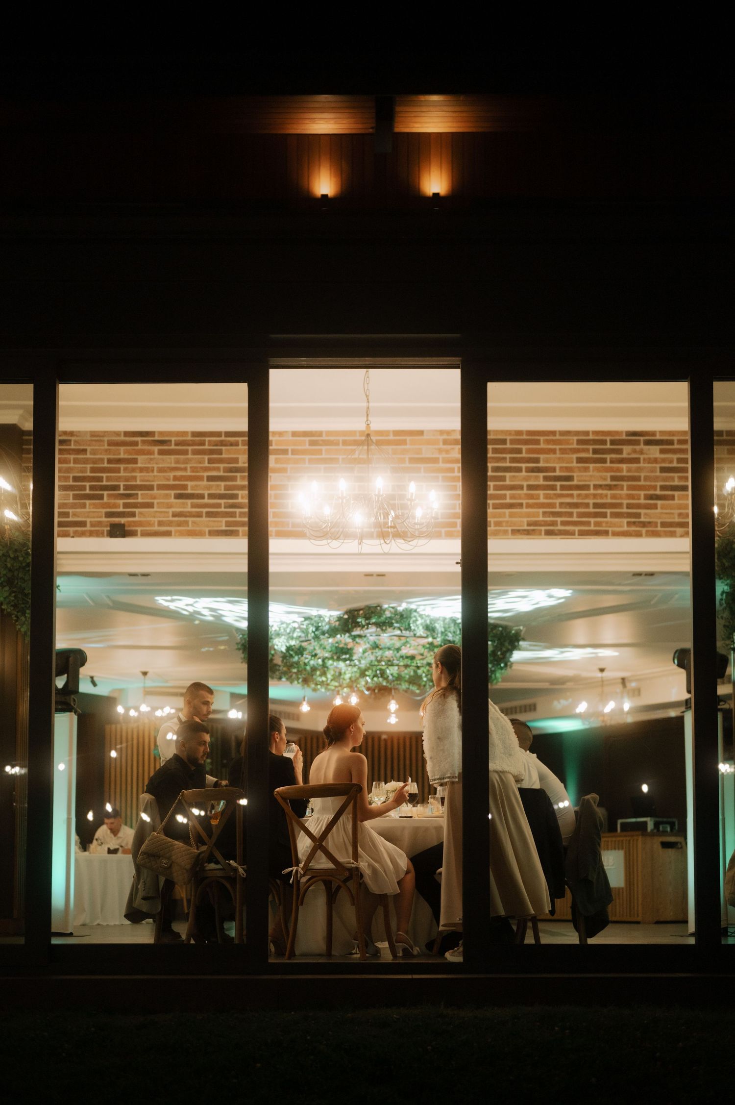 A dimly lit restaurant window at night shows silhouettes of diners and warm interior lighting creating an intimate ambiance.