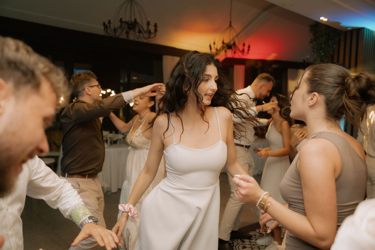 Wedding reception guests dancing together on the dance floor under warm lighting with chandeliers overhead.