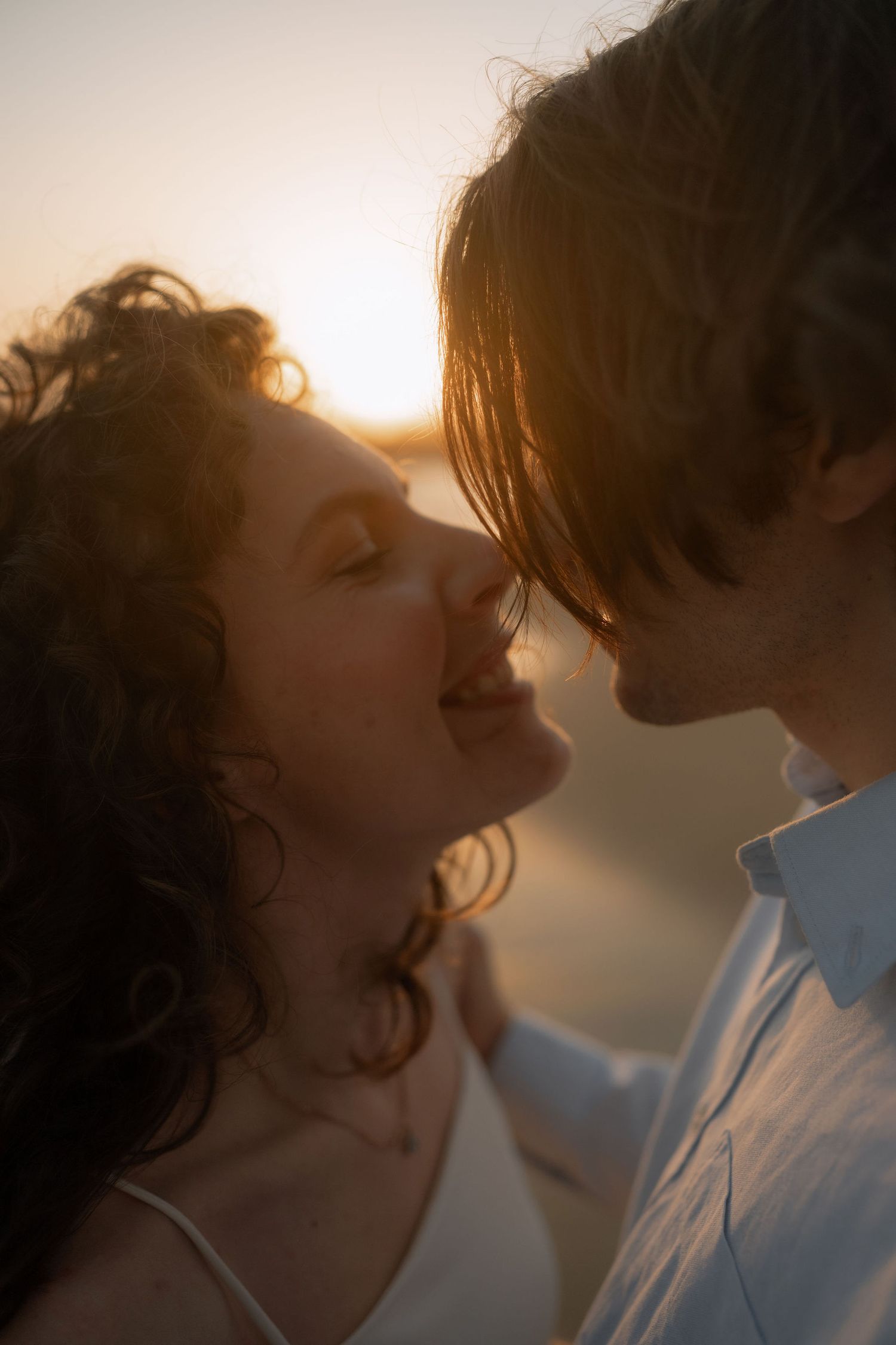 Romantic couple sharing an intimate moment at golden hour sunset, faces close together in a tender embrace.