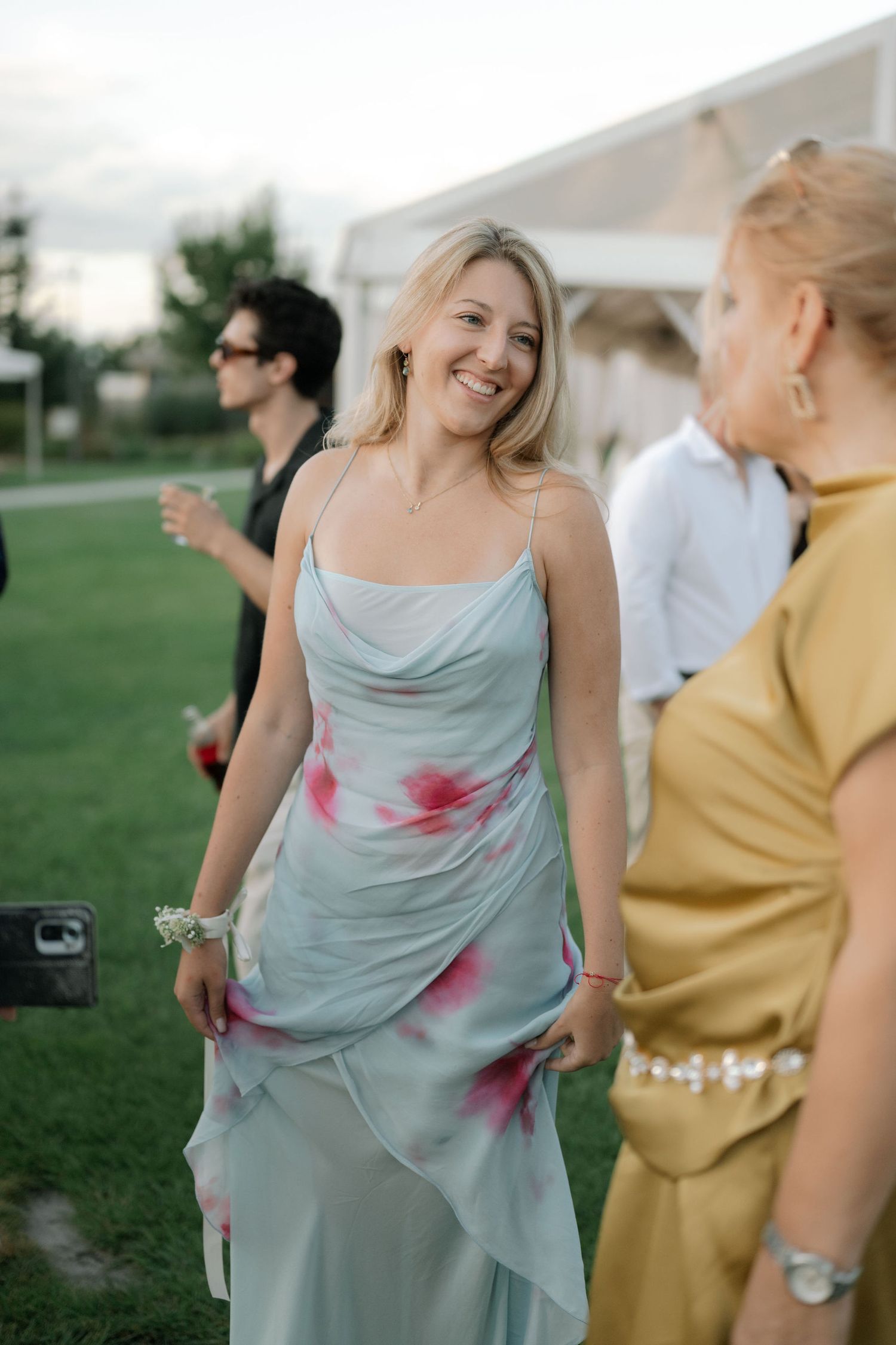 Guests enjoying an outdoor event with a woman in a light blue tie-dye dress smiling at a summer party.