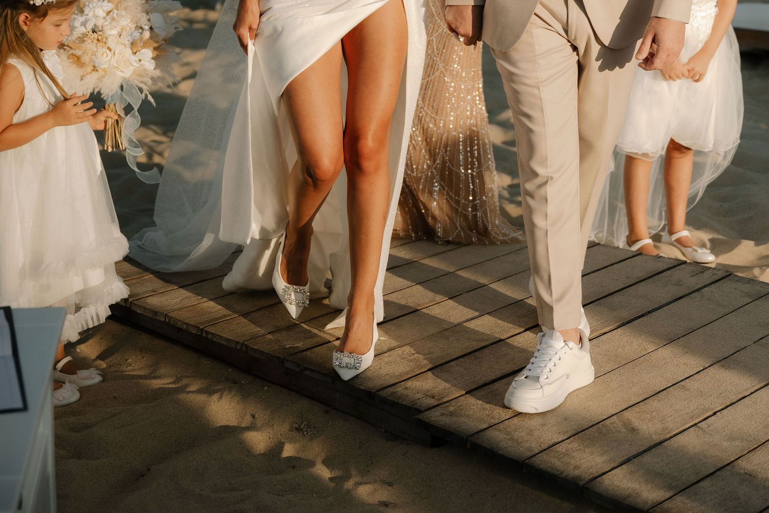 Wedding party members in white outfits and sneakers stand together on a wooden deck during a casual celebration.