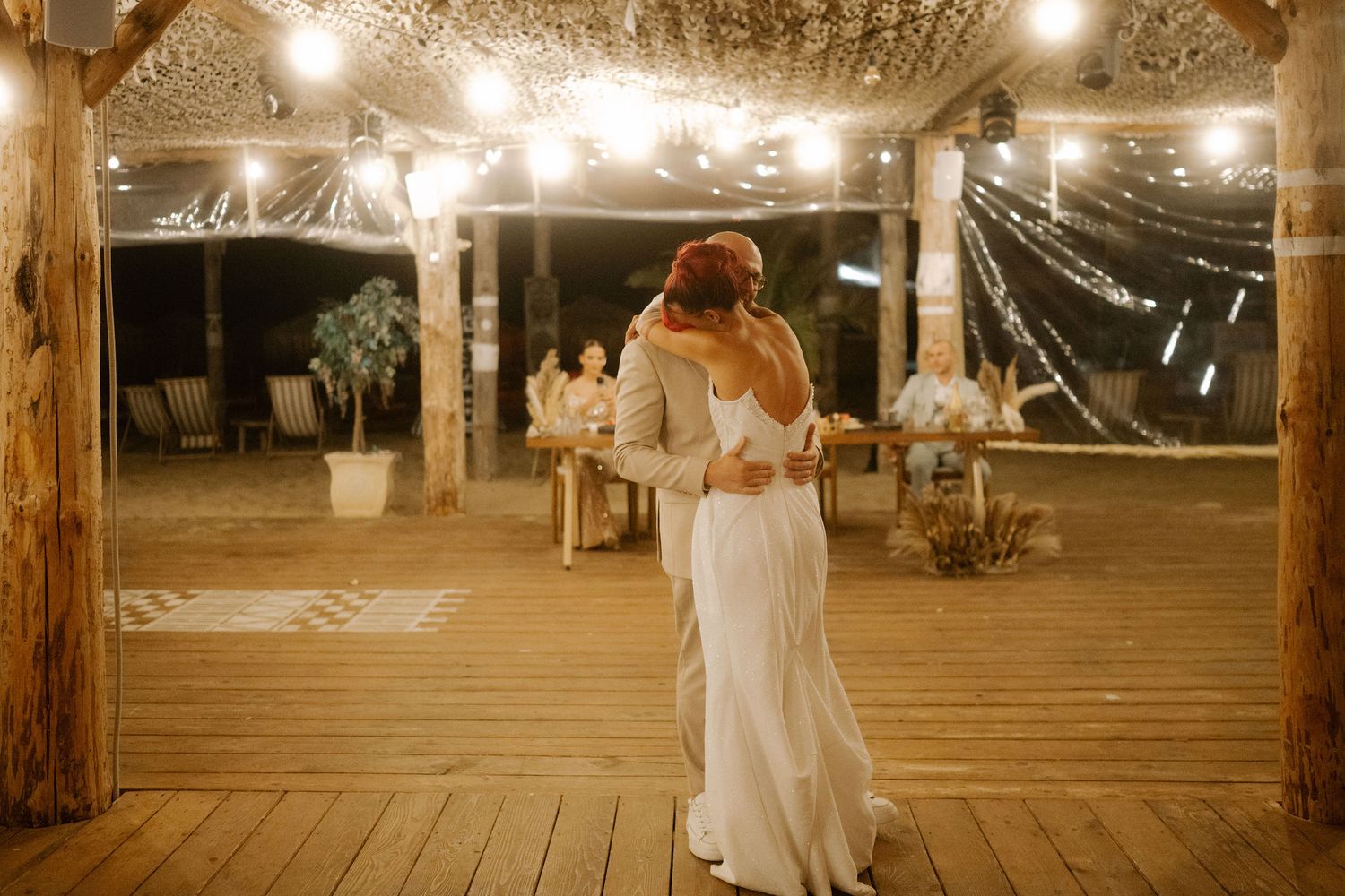 String lights illuminate a rustic wooden barn reception venue with white fabric draping and elegant table settings.