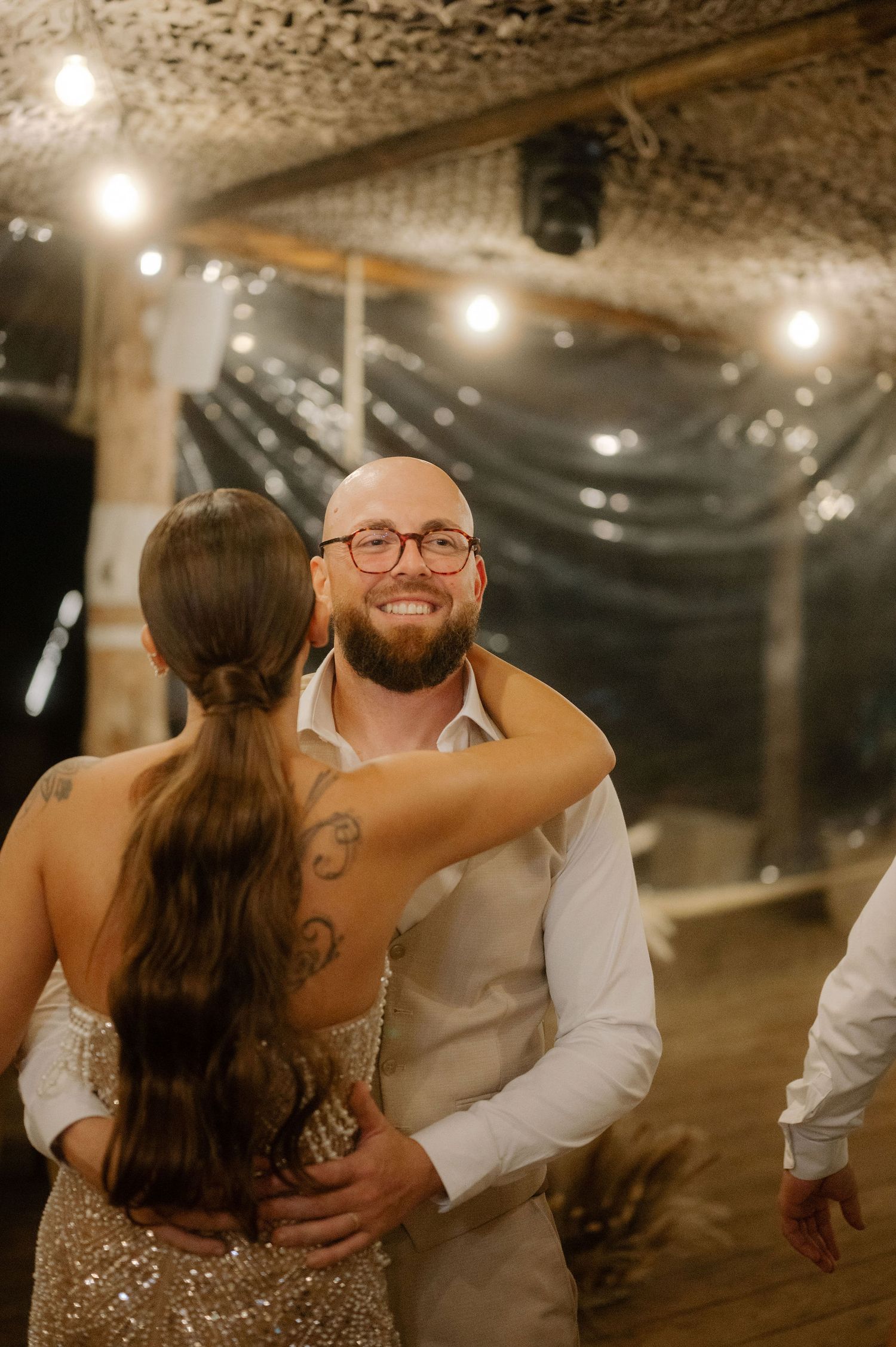 Couple shares intimate dance moments at rustic indoor wedding reception with string lights overhead.