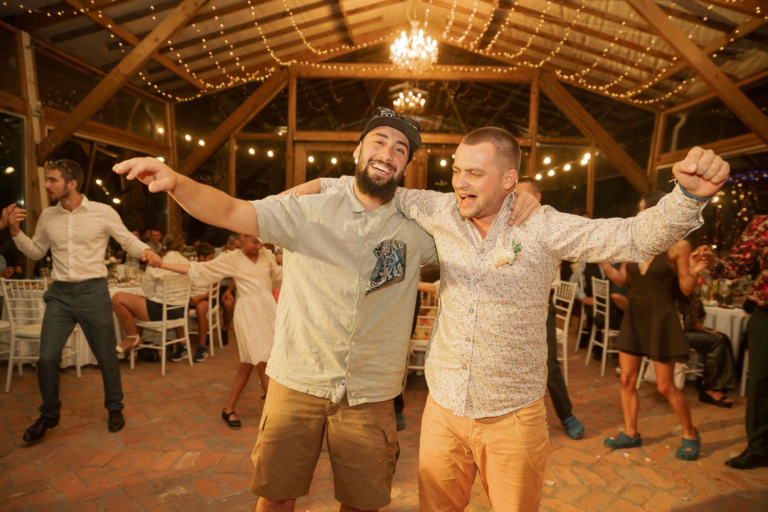 Wedding guests dance together under twinkling lights at a rustic barn reception venue.