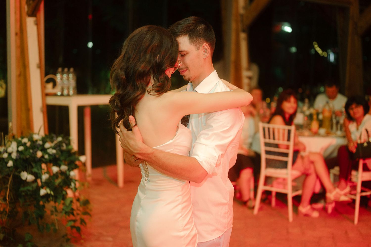 A couple dances together on a warm-lit dance floor during a wedding reception.