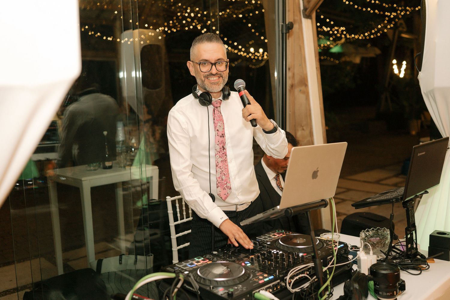 A DJ performs at a wedding reception with string lights and decorations in the background.
