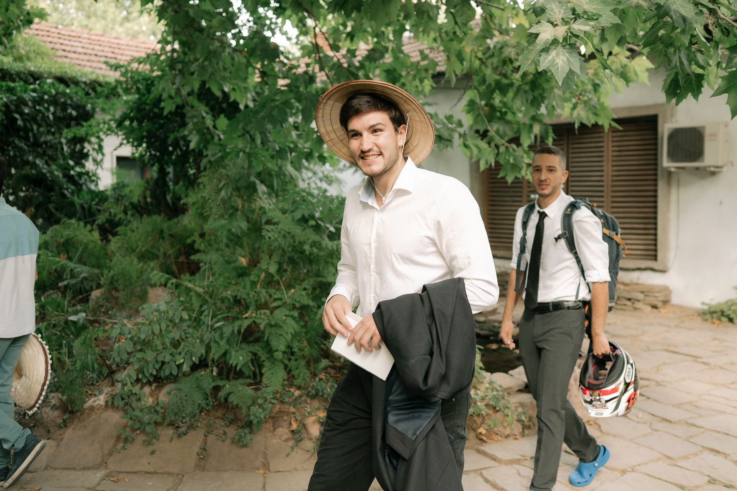 Students in graduation attire walk and pose together under green trees on a sunny day.