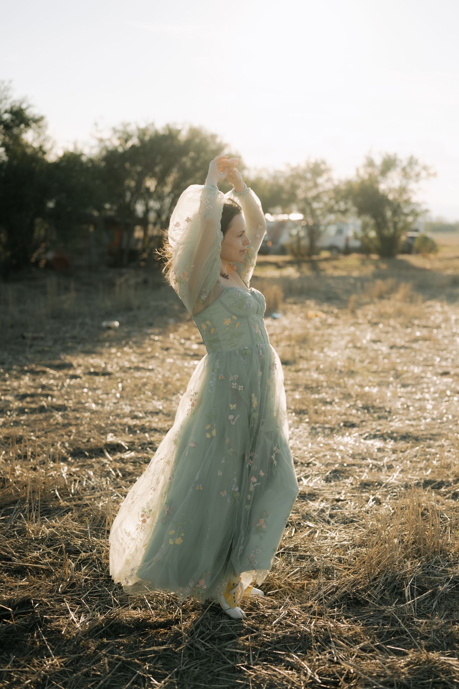 A dreamy sunset photoshoot features an ethereal blue dress flowing in the golden light across a rustic field.