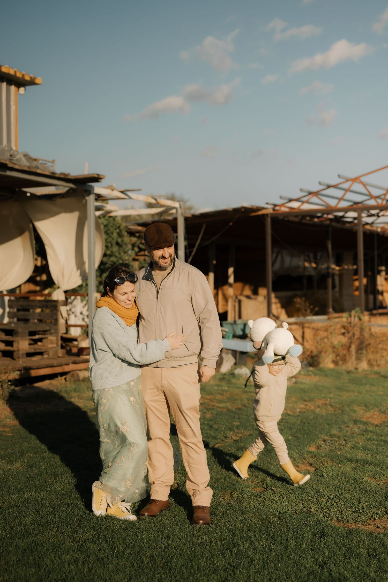 A couple shares a tender moment together on a grassy lawn during golden hour with rustic buildings in the background.