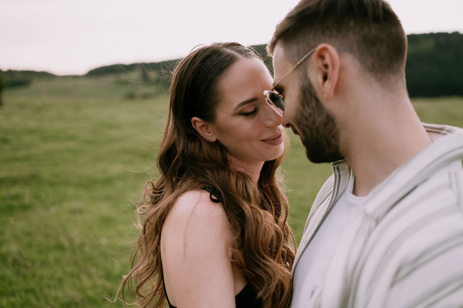 A couple shares romantic moments together in a green field during a sunny outdoor photo session.