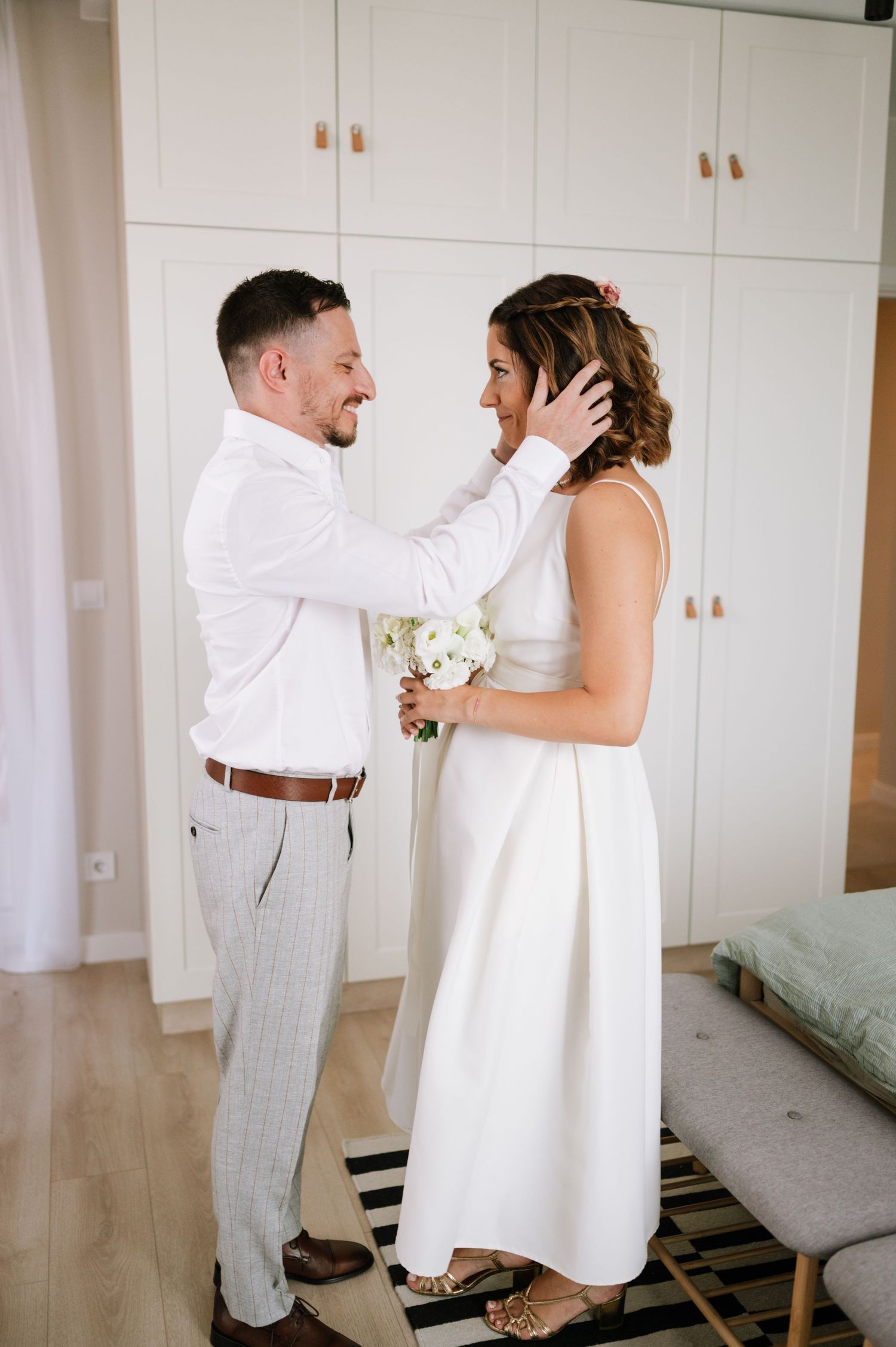 A couple shares tender moments during their first look wedding photos in a bright white room.