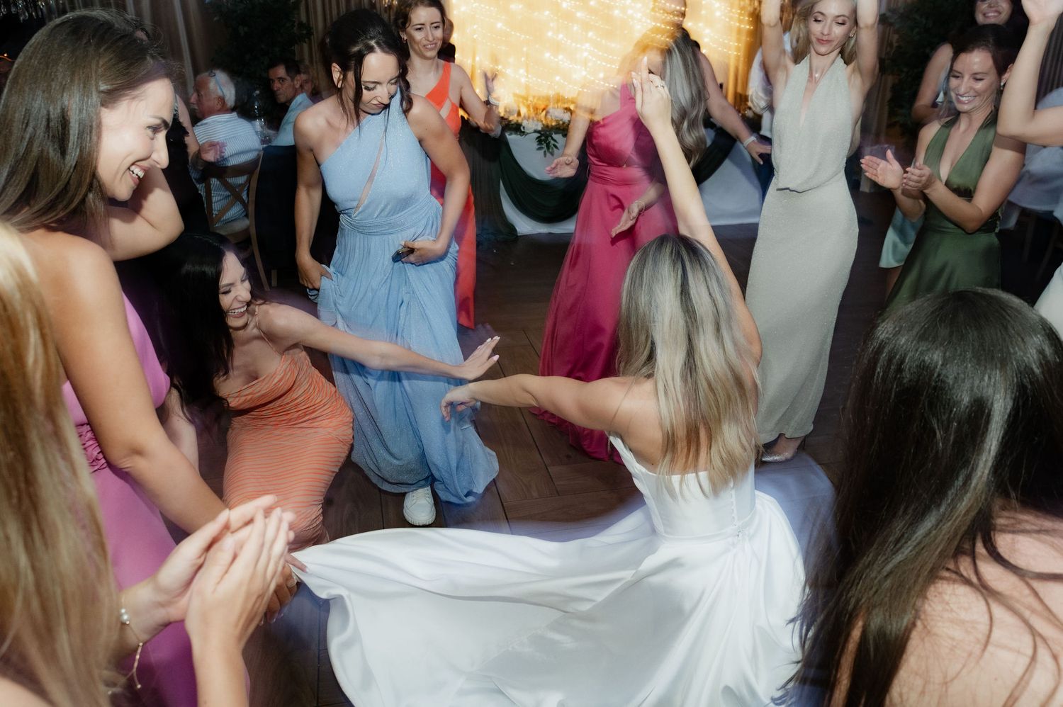 A lively crowd dances and socializes at a dimly lit party venue with warm lighting and festive atmosphere.