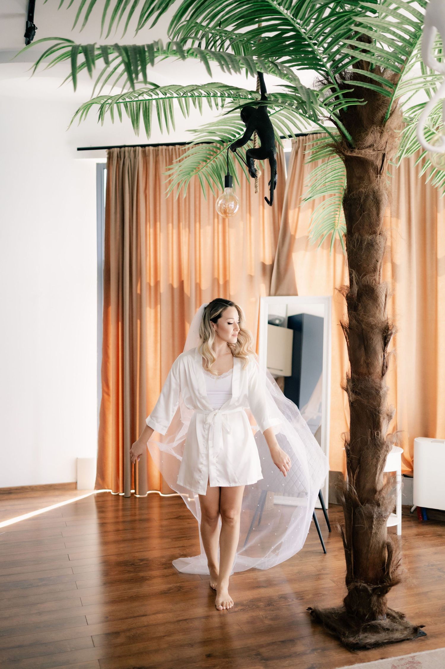 An ethereal bridal photoshoot featuring delicate movements near an indoor palm tree with orange curtains.