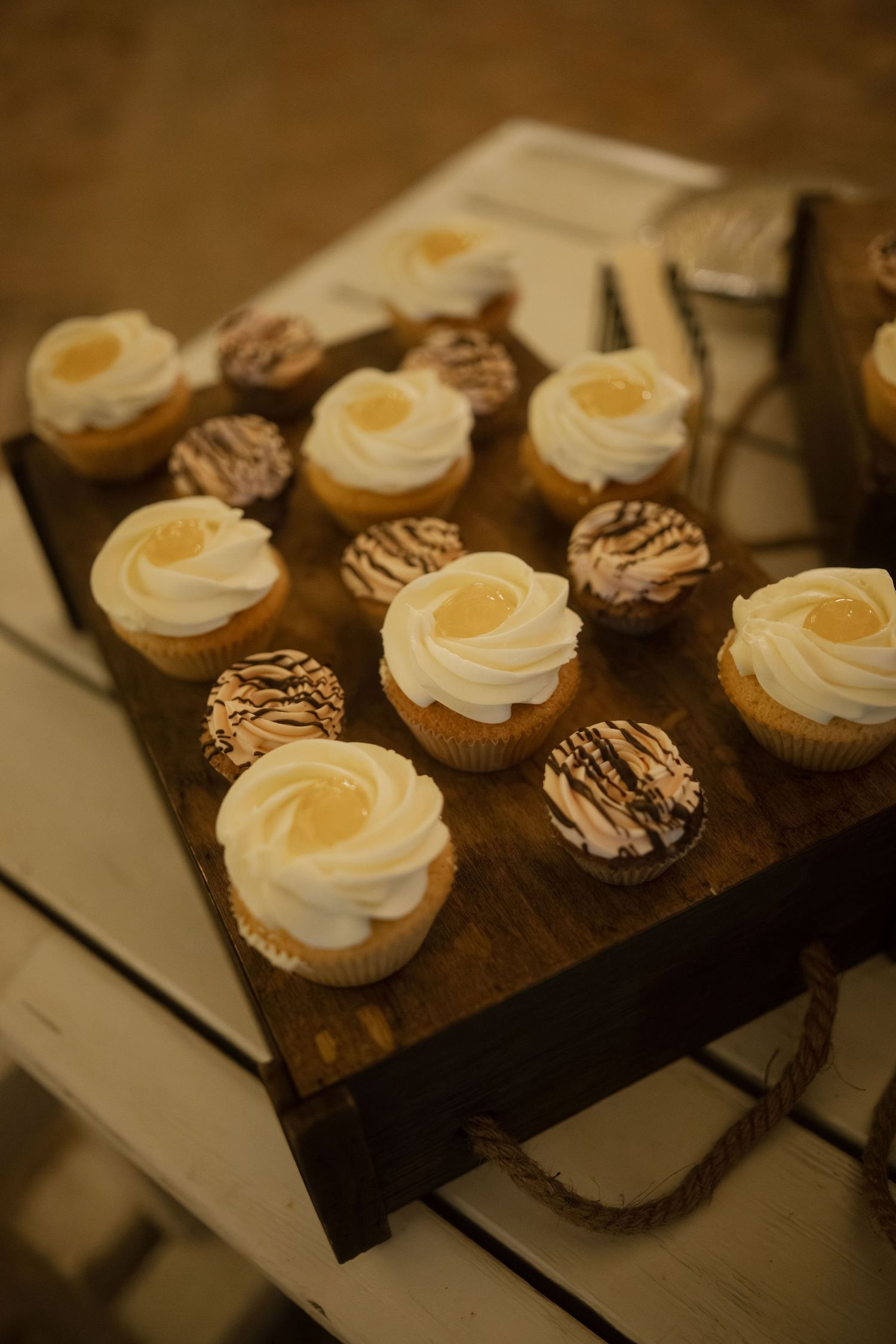 Chocolate and vanilla cupcakes arranged on a rustic wooden serving board in warm lighting.