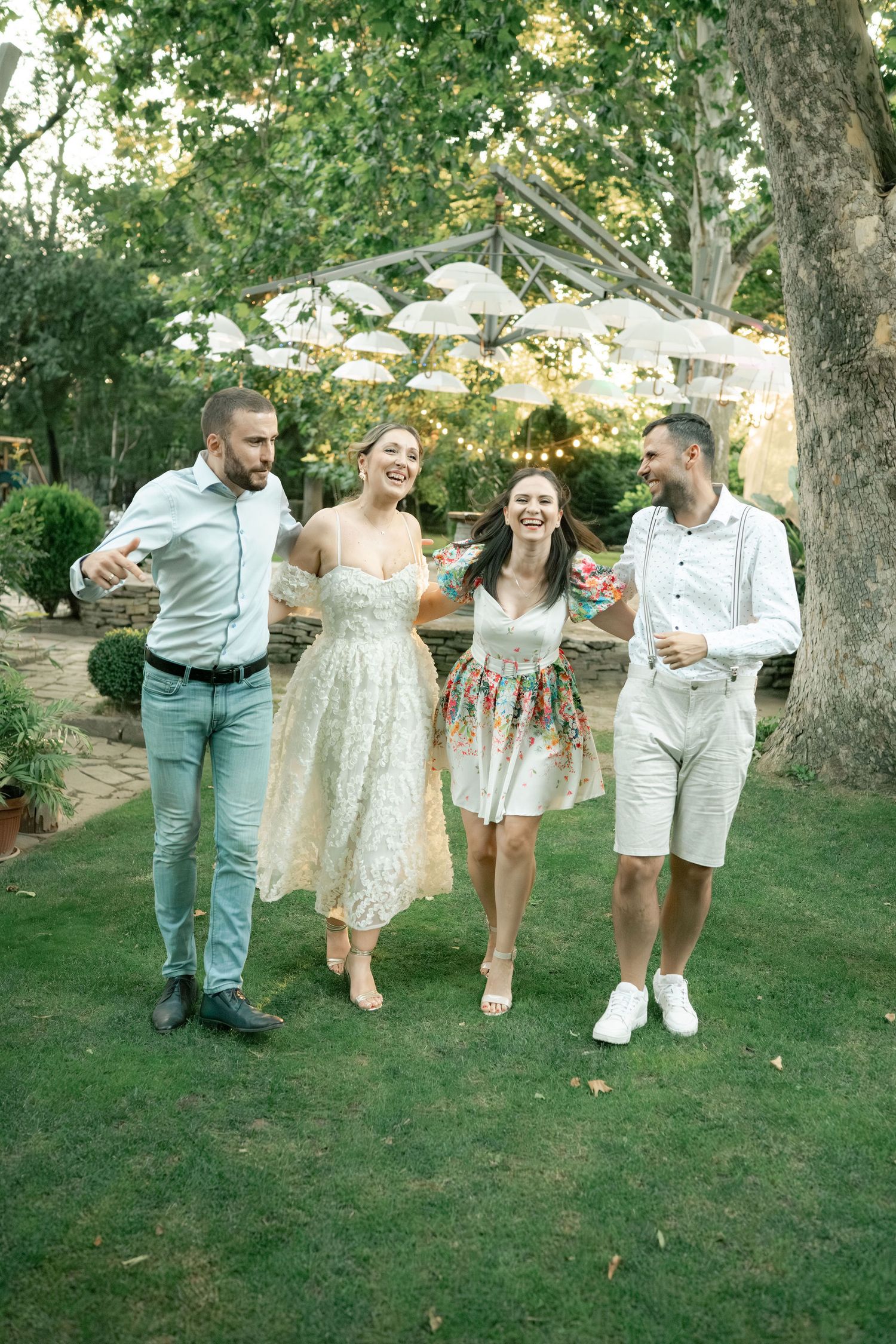 A group in coordinated white and cream outfits poses playfully on a grassy lawn during golden hour.