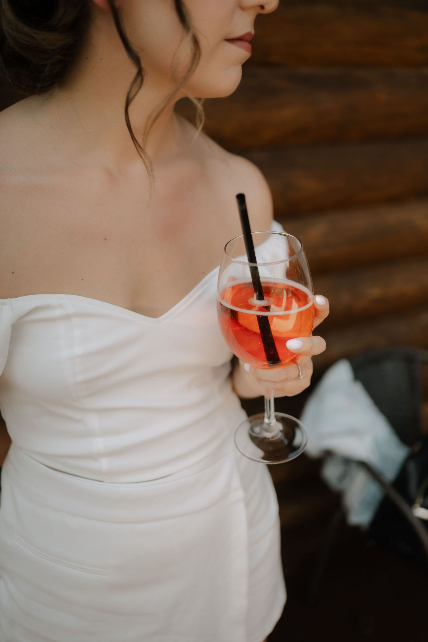Close-up view of a white dress and pink cocktail against wooden cabin walls.