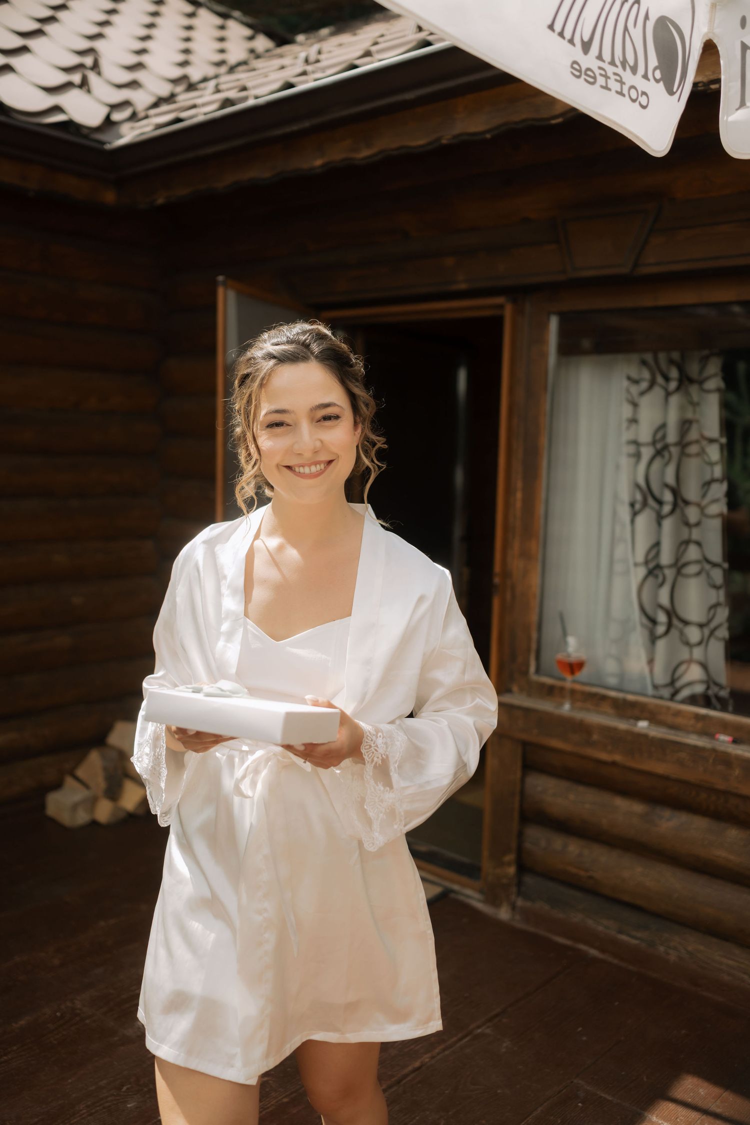 Someone wearing a white satin robe holds a plate while standing on the porch of a rustic wooden cabin.