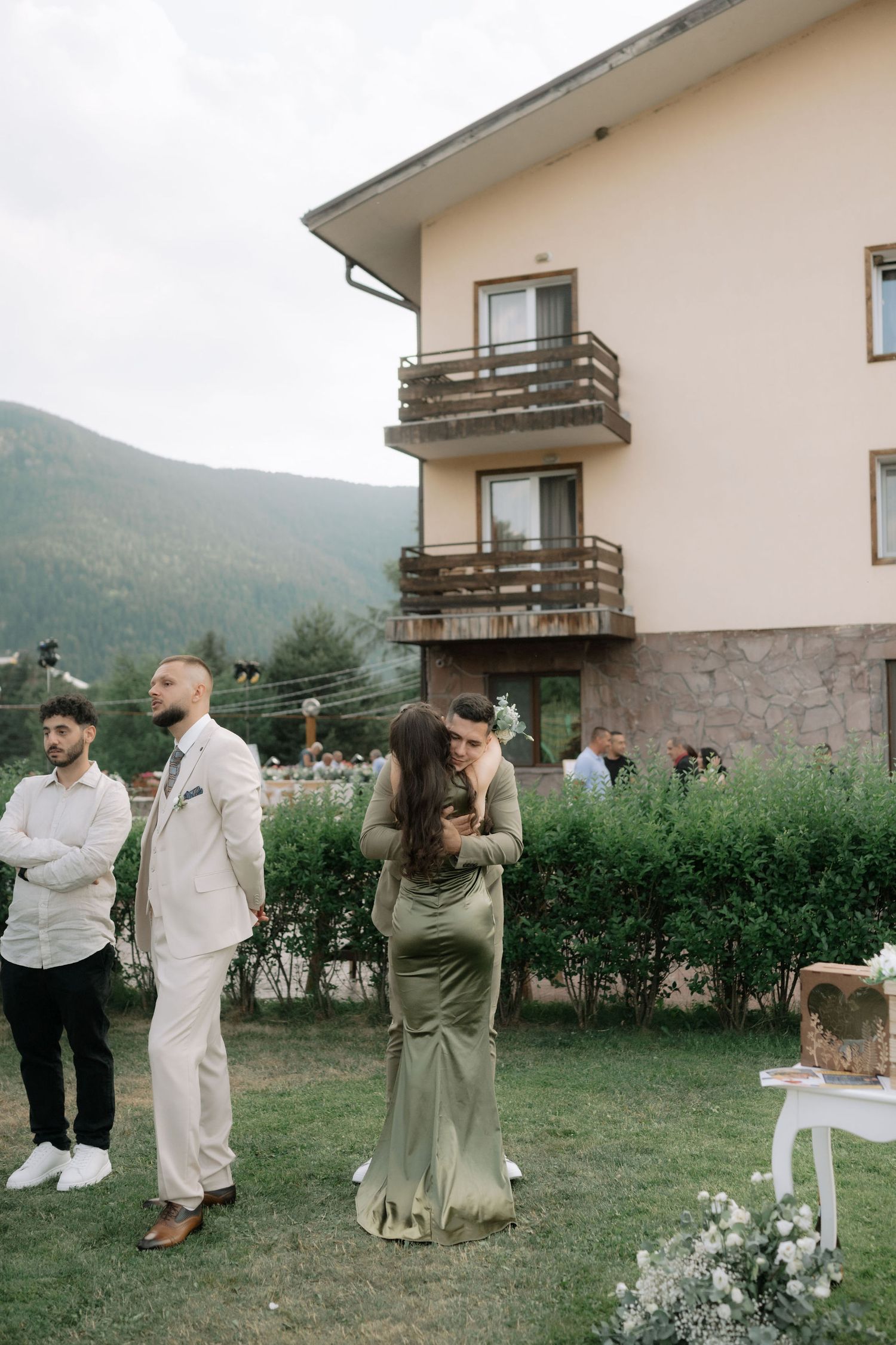Wedding guests gather in a garden setting beside a mountain house during an outdoor celebration.