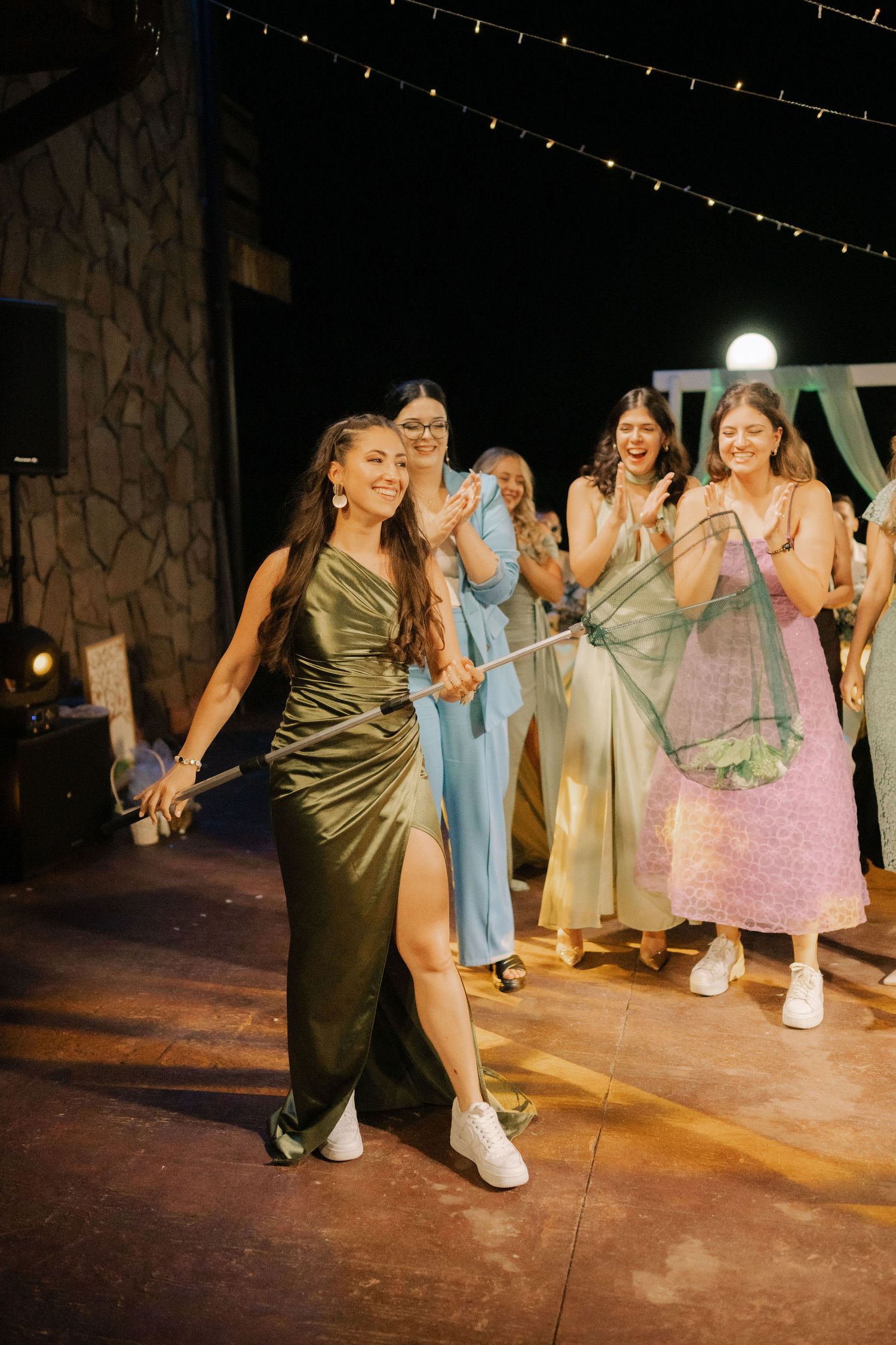 A group of wedding guests dance energetically on an outdoor stone patio during an evening reception celebration.