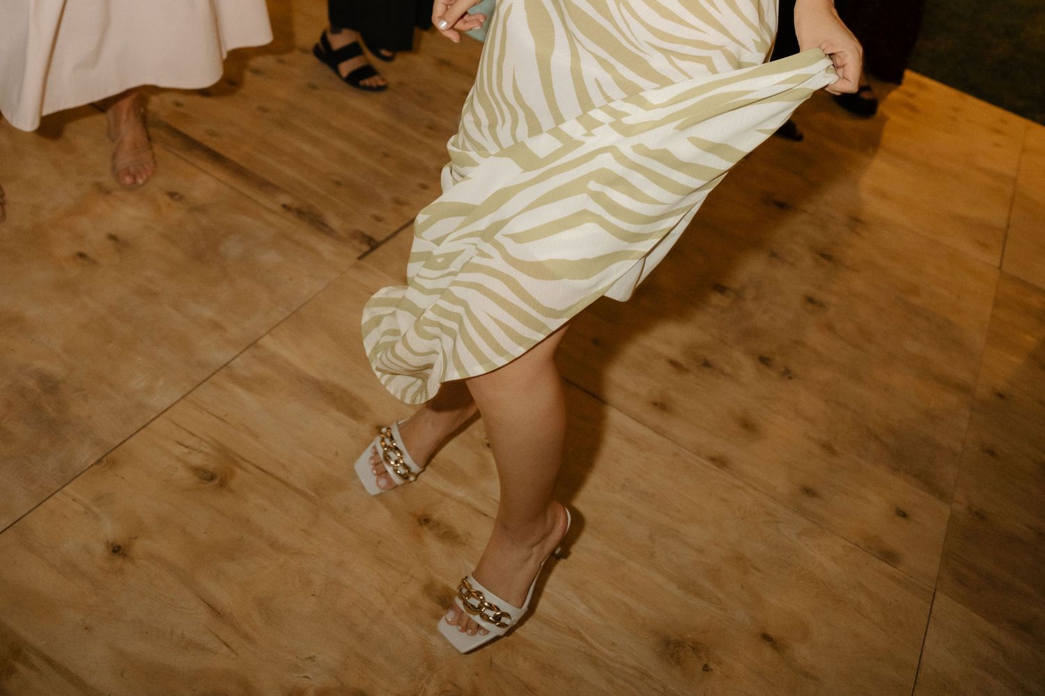 A person's feet in silver sandals walking across a wooden floor in a sequence of steps.