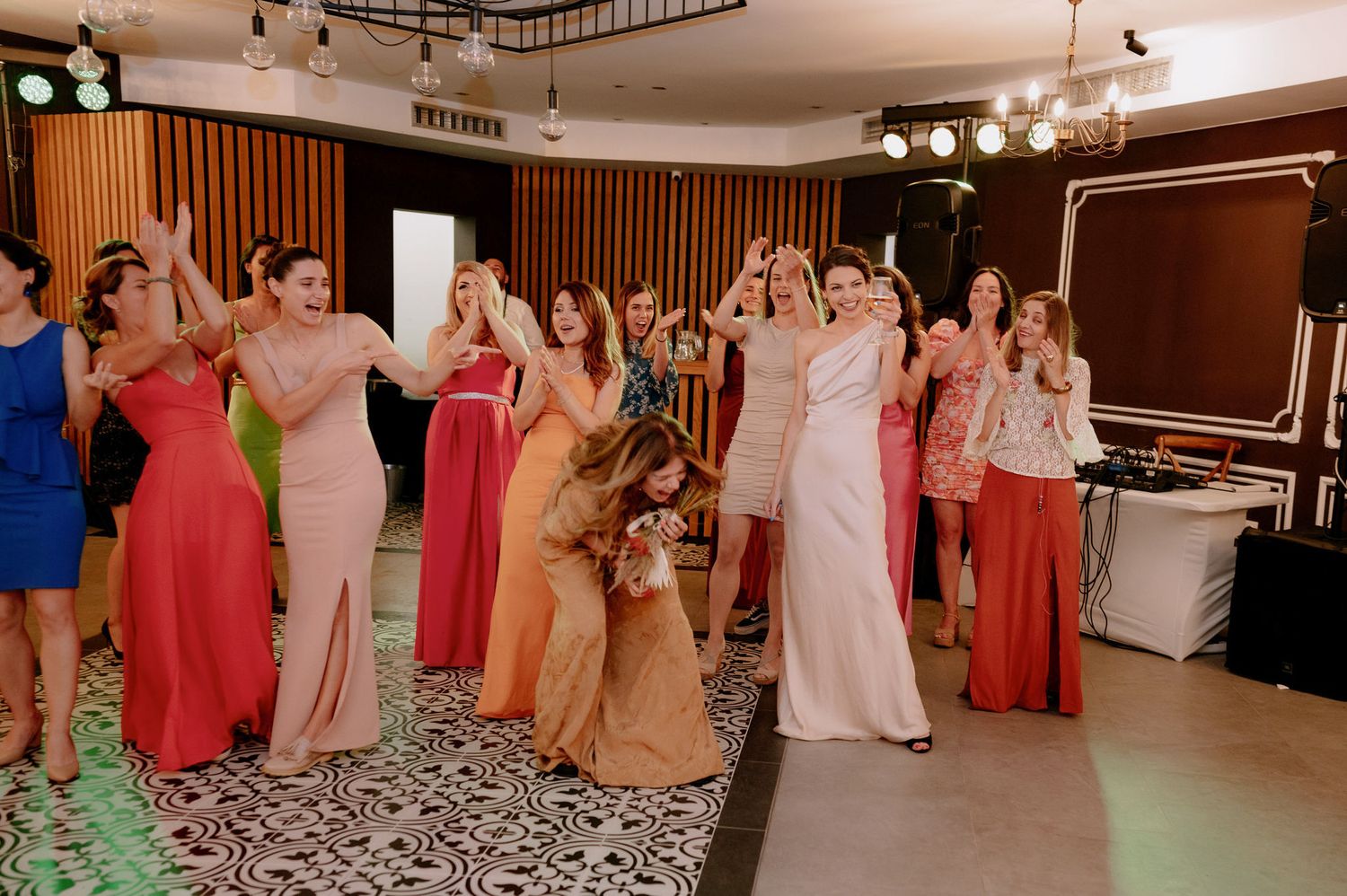 Wedding guests dance and celebrate together in a reception hall with colorful dresses and festive lighting.