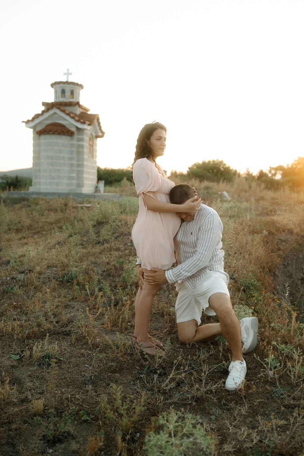 A romantic couple embraces on a grassy hillside at sunset, creating a dreamy silhouette against the golden sky.