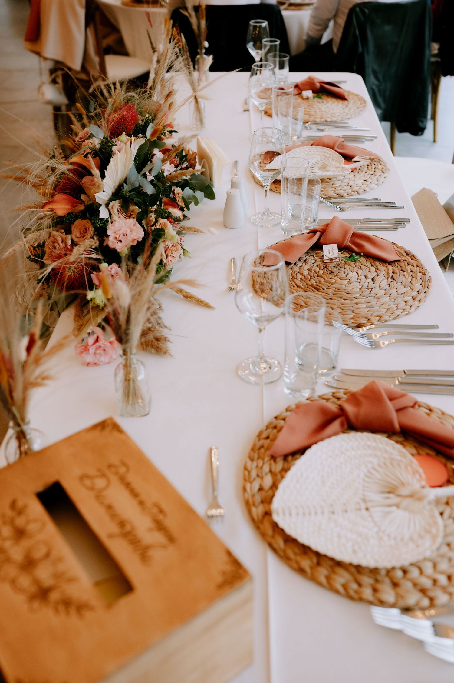 Elegant wedding table setting with coral napkins, woven placemats, wine glasses and romantic floral centerpiece.
