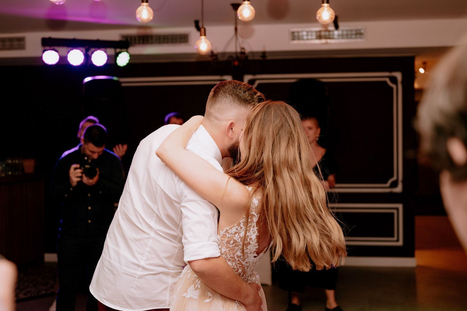 Wedding couple shares an intimate dance together on a dimly lit dance floor with purple lighting in the background.