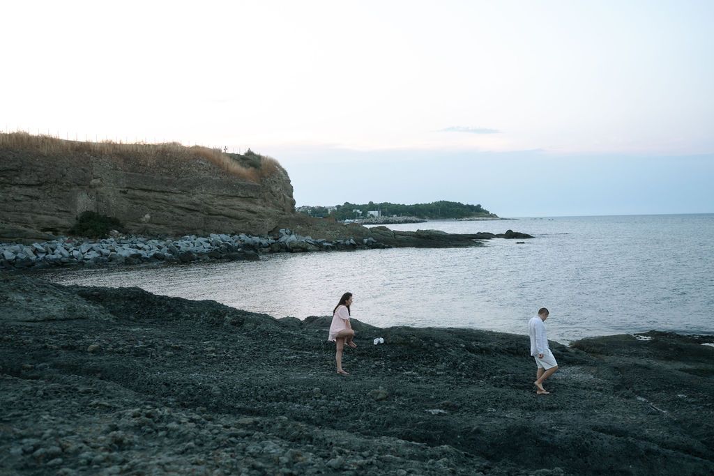 People explore a dramatic black volcanic beach coastline with rocky cliffs and ocean views in Hawaii at sunset.