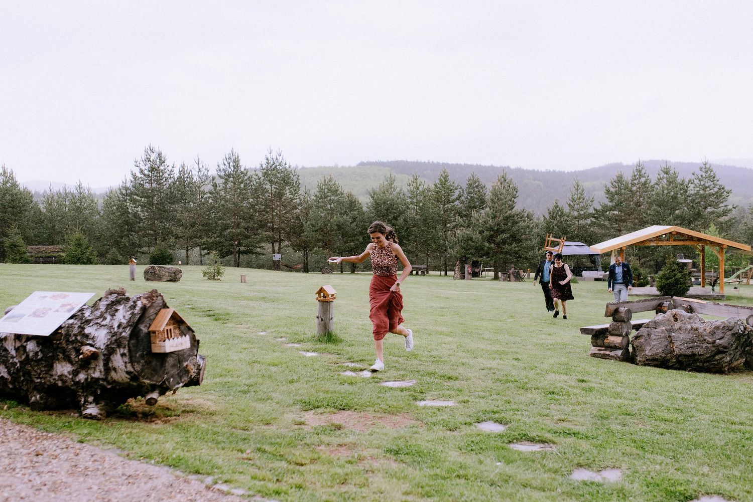 People playing and running on a grassy field with mountains and trees in the background.