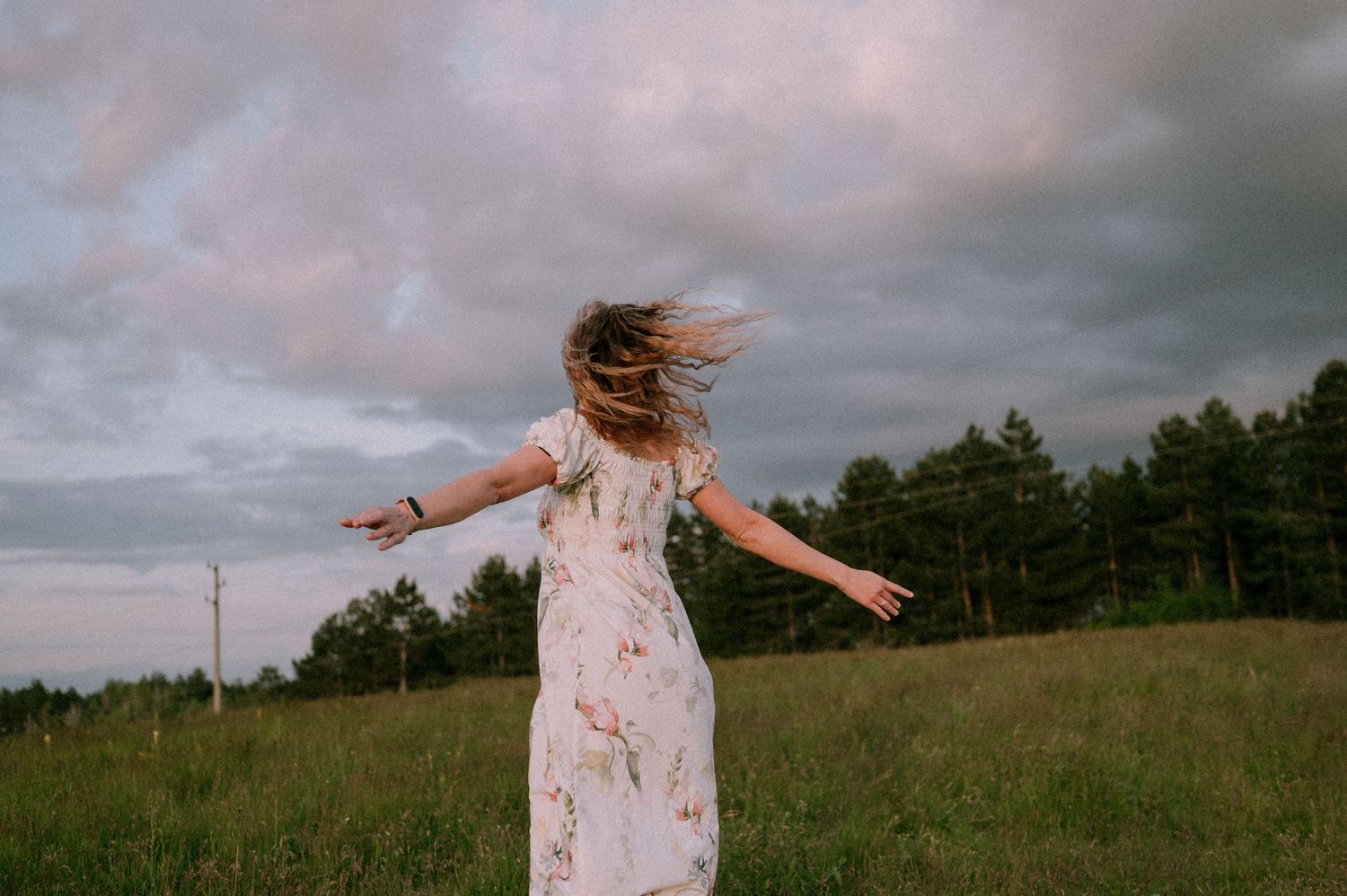 A person spins freely in a grassy field under dramatic cloudy skies.