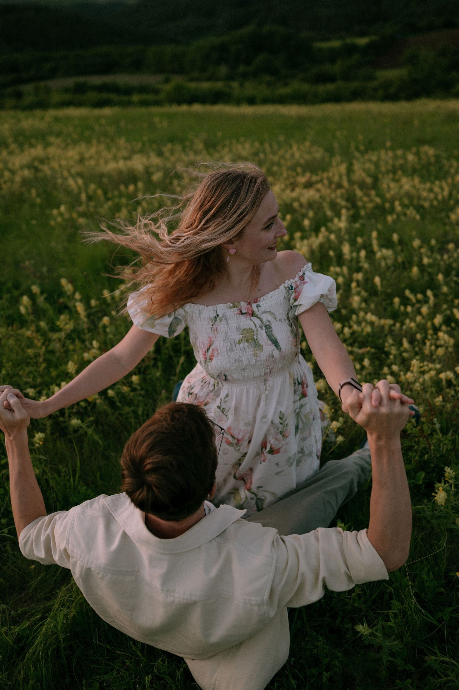 A couple spins and dances through a field of yellow wildflowers against a scenic landscape.